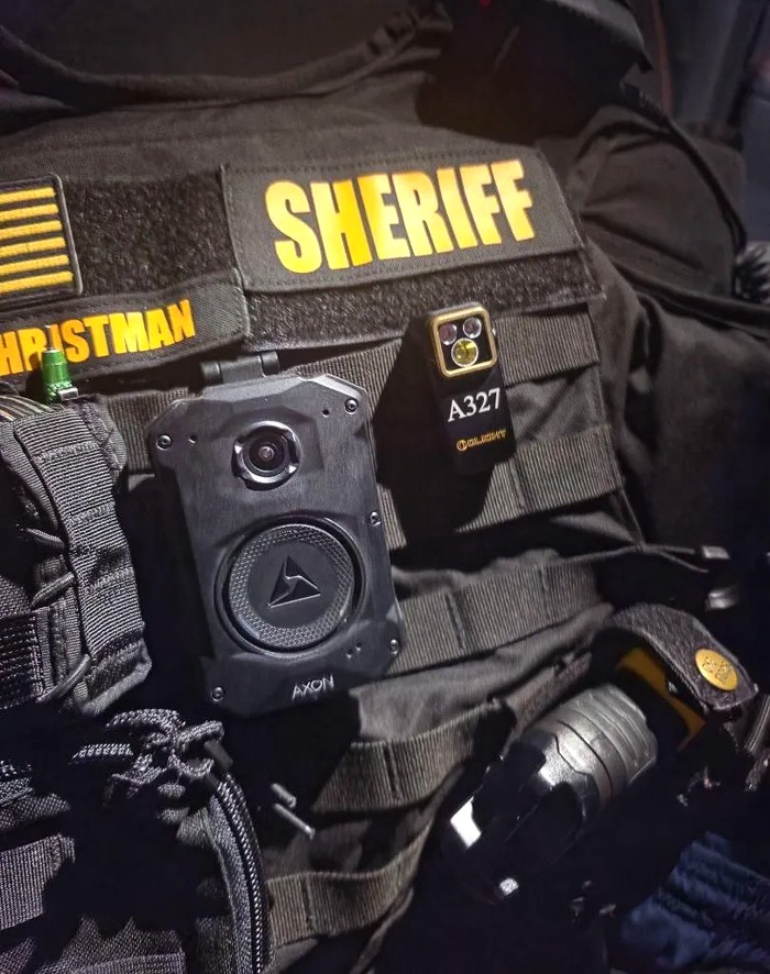 Sheriff's tactical vest with an Olight Oclip engraved with badge number A327, mounted beside a body camera