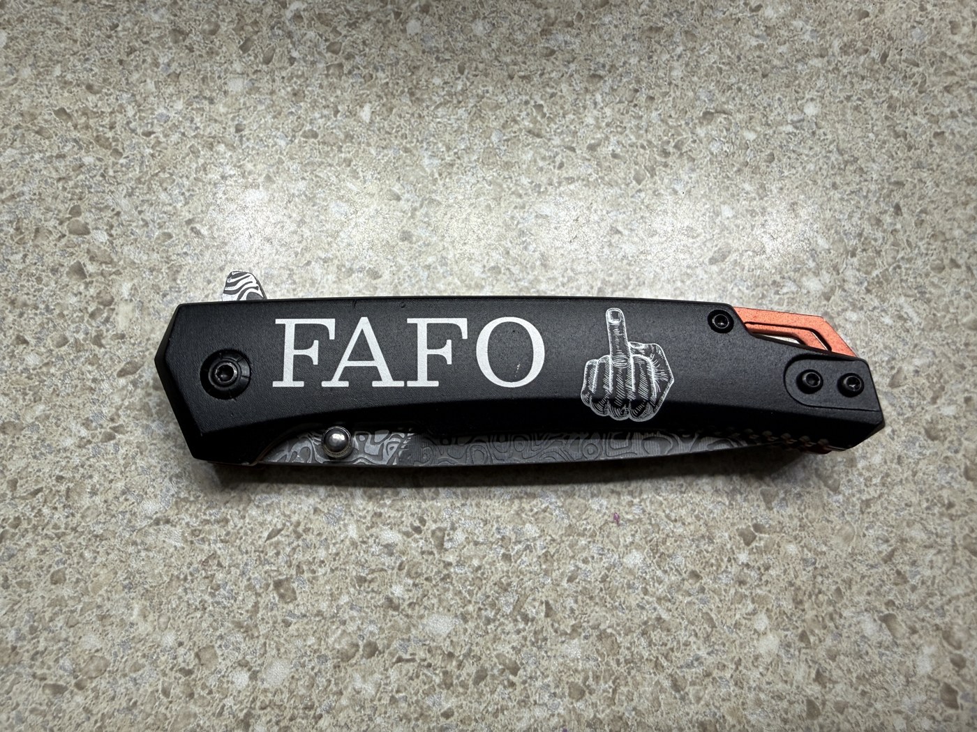 Black folding knife closed, handle engraved FAFO with a hand gesture graphic