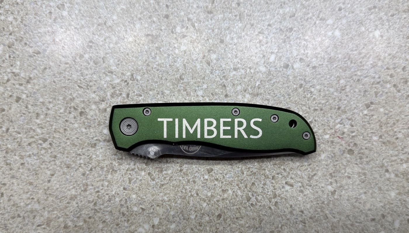 Green folding knife handle laser engraved with the name TIMBERS in block letters
